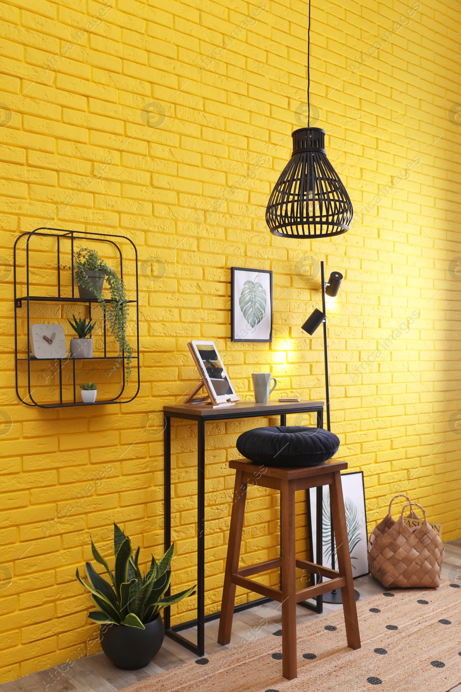 Photo of High wooden table with tablet and stool as stand up workplace near yellow brick wall. Stylish interior