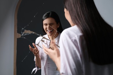 Mental problems. Young woman laughing near broken mirror indoors