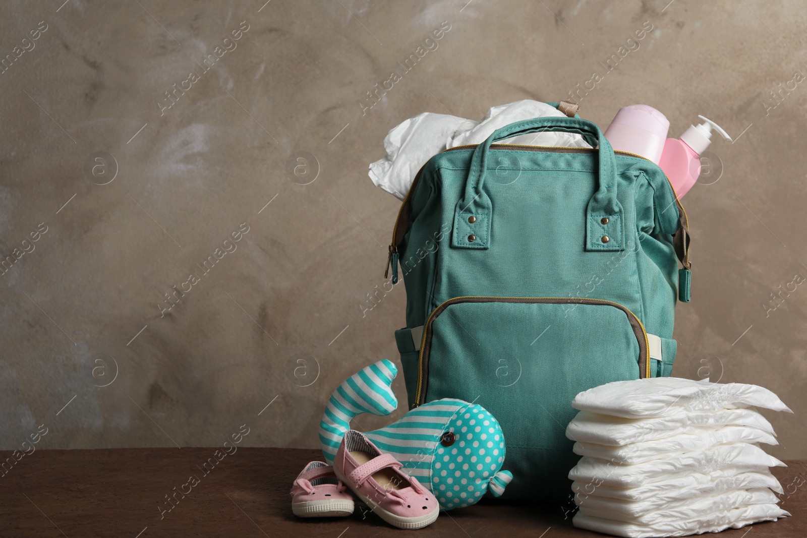 Photo of Bag with diapers and baby accessories on wooden table. Space for text