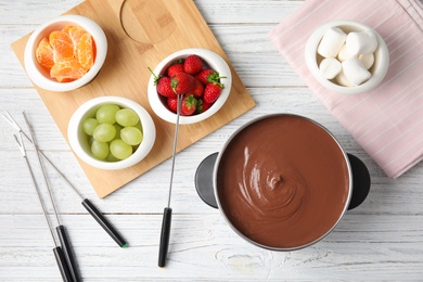 Flat lay composition with chocolate fondue in pot and fruits on wooden background