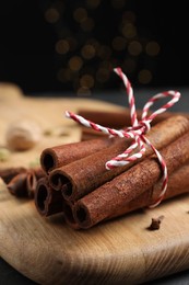 Cinnamon sticks and other spices on table against black background with blurred lights, closeup