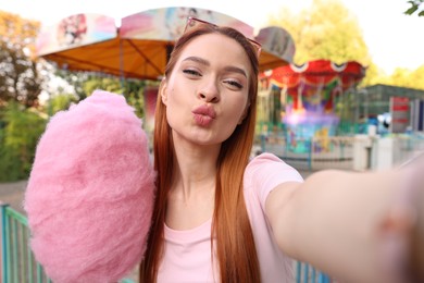 Photo of Funny woman with cotton candy taking selfie at funfair