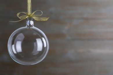 Photo of Transparent glass Christmas ball with golden ribbon and bow on blurred background. Space for text