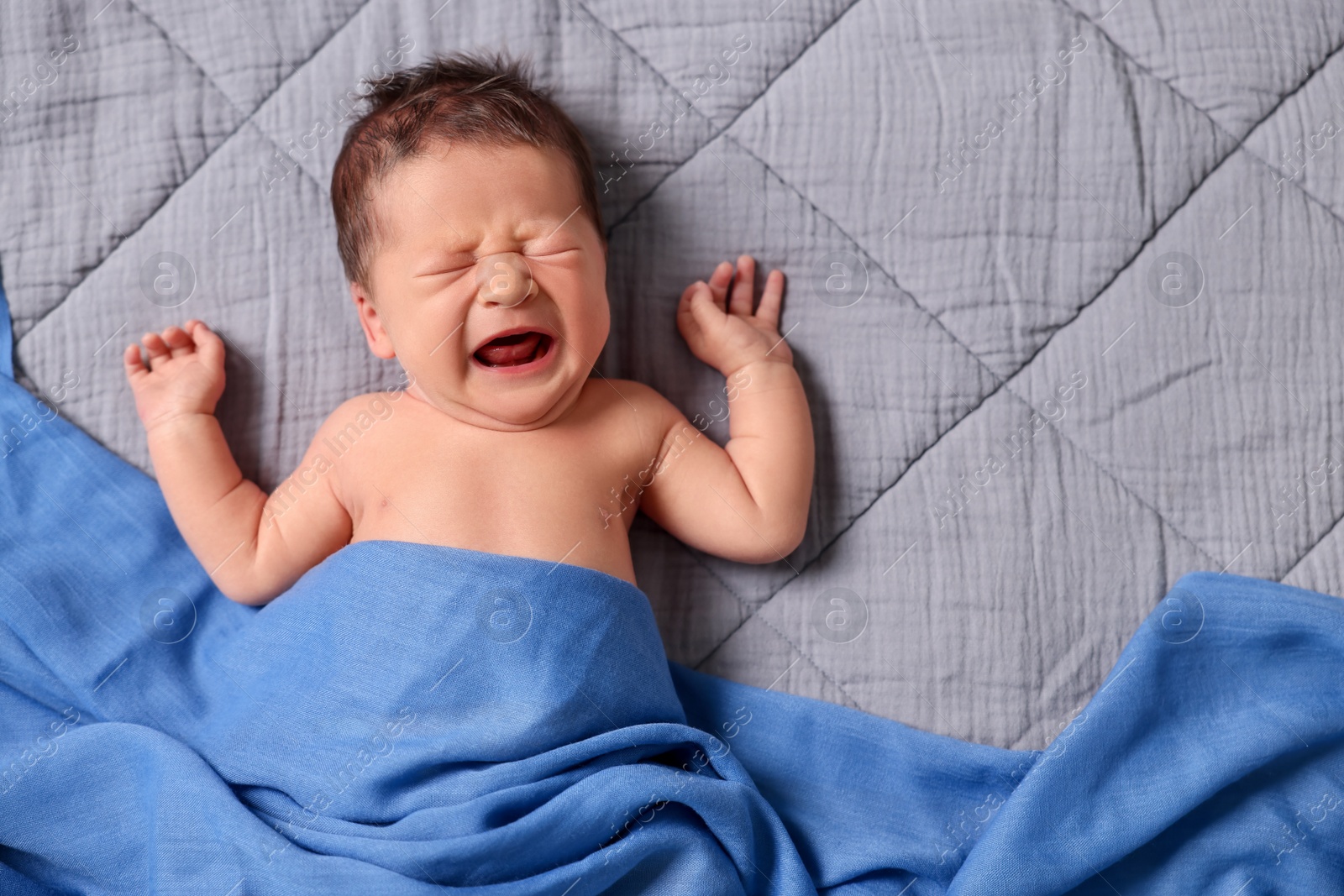 Photo of Adorable newborn baby crying under blue blanket on bed, top view. Space for text