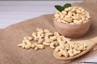 Photo of Tasty cashew nuts and green leaves on table, closeup. Space for text