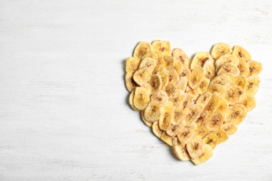 Photo of Heart shape made of sweet banana slices on wooden table, top view with space for text. Dried fruit as healthy snack