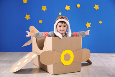 Cute little child playing with cardboard airplane near blue wall