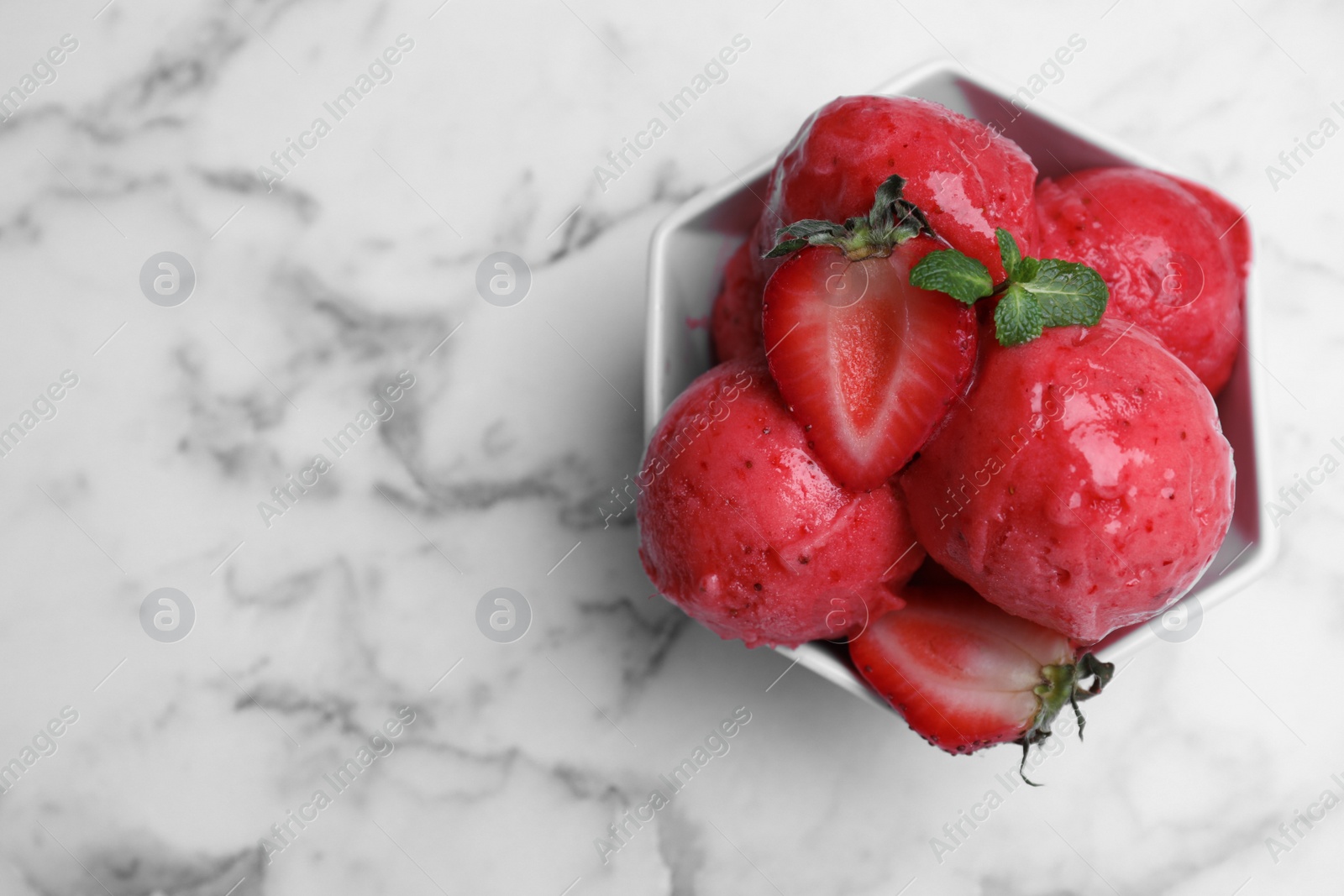 Photo of Yummy strawberry ice cream in bowl on white marble table, top view. Space for text