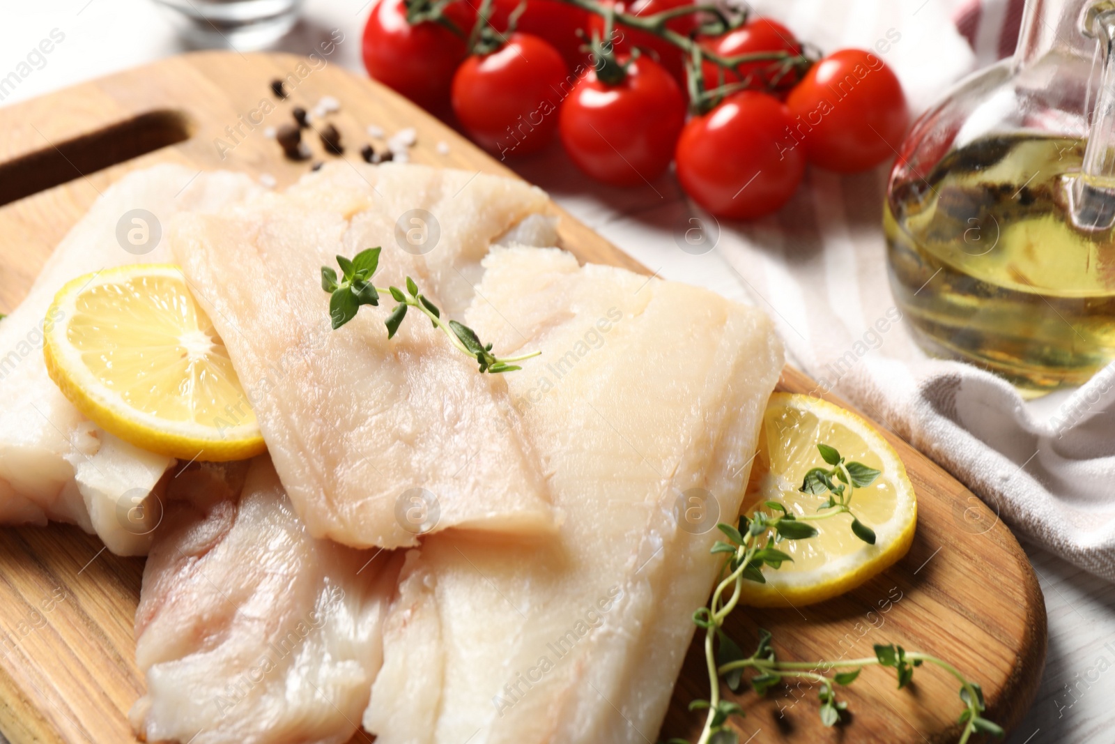 Photo of Pieces of raw cod fish, lemon, tomatoes and oil on table, closeup