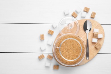 Photo of Brown sugar in jar and spoon on white wooden table, top view. Space for text