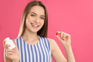Young woman with vitamin pill on pink background