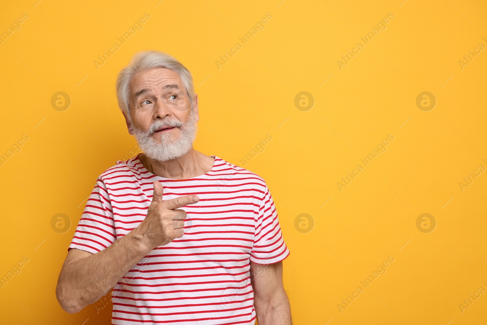 Photo of Senior man with mustache pointing at something on orange background, space for text