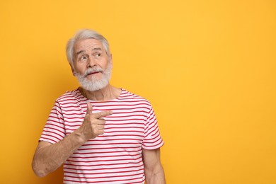 Senior man with mustache pointing at something on orange background, space for text