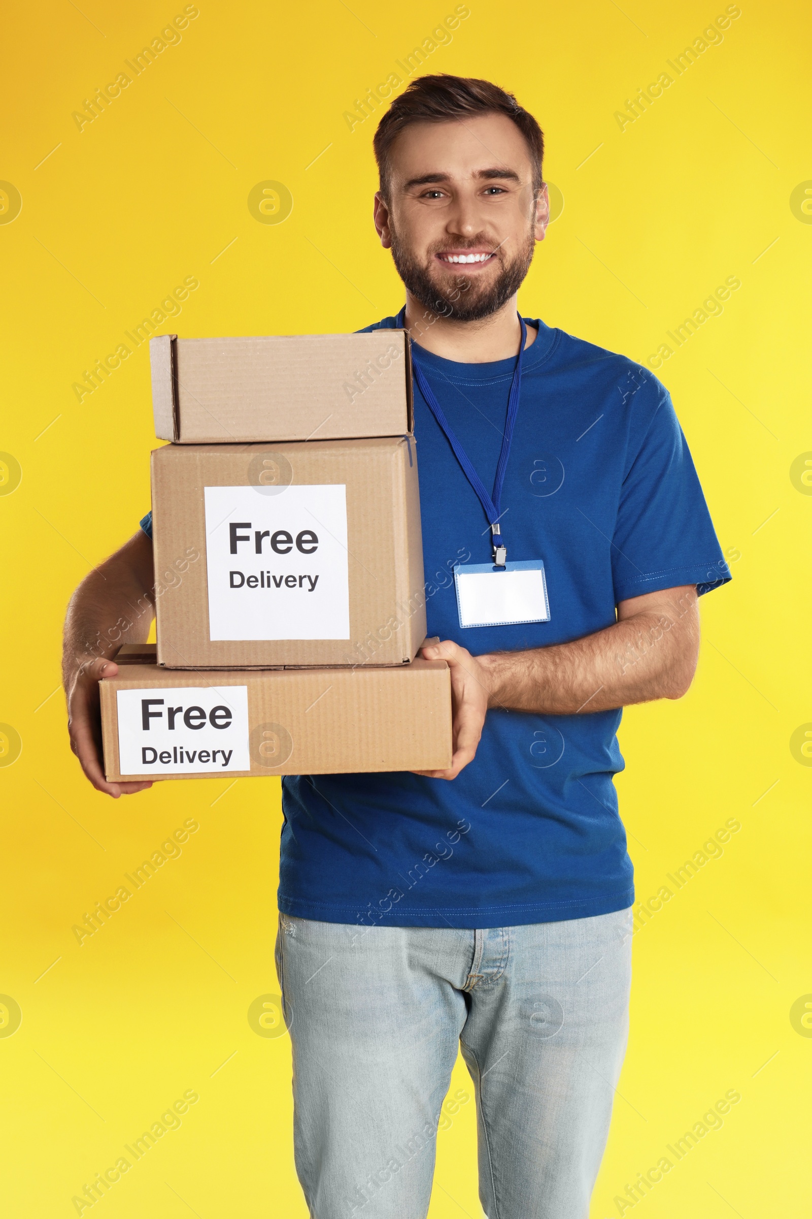 Photo of Male courier holding parcels with stickers Free Delivery on yellow background