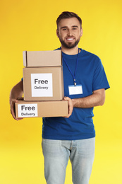 Photo of Male courier holding parcels with stickers Free Delivery on yellow background