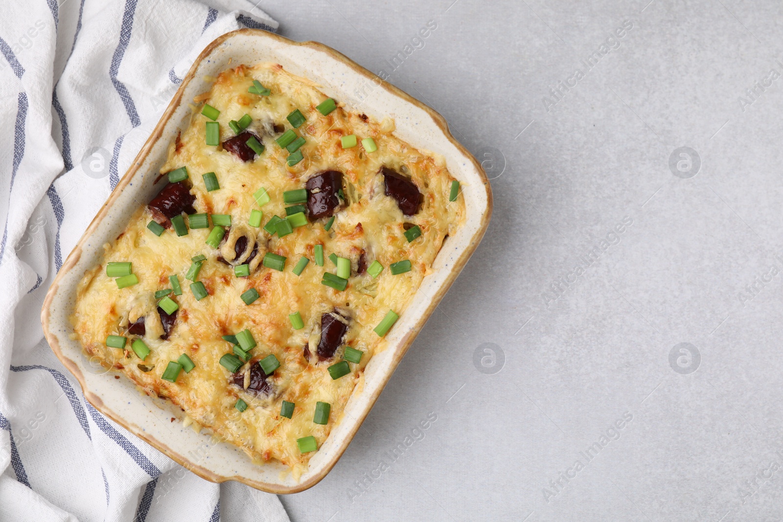 Photo of Tasty sausage casserole with green onions in baking dish on white table, top view. Space for text