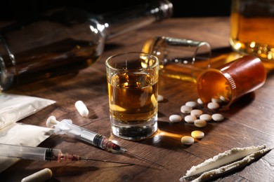 Photo of Alcohol and drug addiction. Whiskey in glass, syringes, pills and cocaine on wooden table