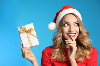 Photo of Happy young woman wearing Santa hat with Christmas gift on light blue background