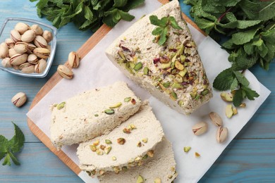 Photo of Pieces of tasty halva with pistachios and mint on light blue wooden table, flat lay