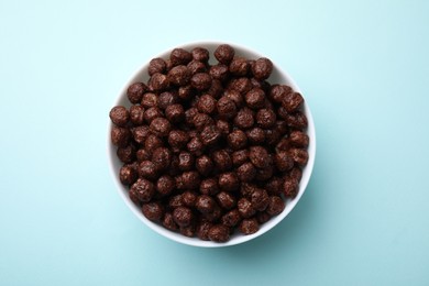 Photo of Chocolate cereal balls in bowl on light blue table, top view