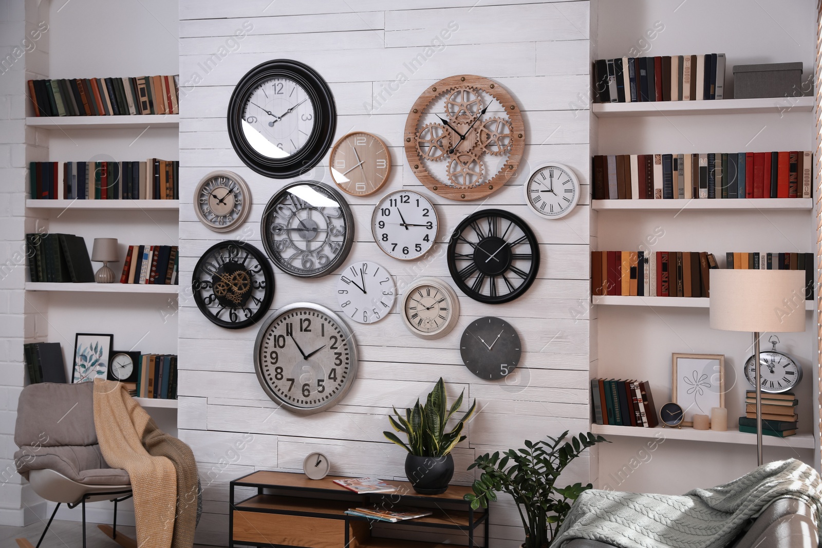 Photo of Stylish room interior with console table, comfortable furniture and collection of different clocks on white wall