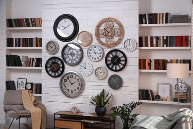 Photo of Stylish room interior with console table, comfortable furniture and collection of different clocks on white wall