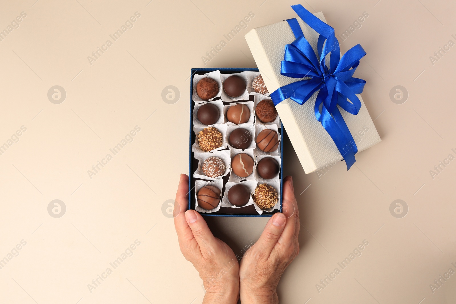 Photo of Woman with box of delicious chocolate candies on beige background, top view
