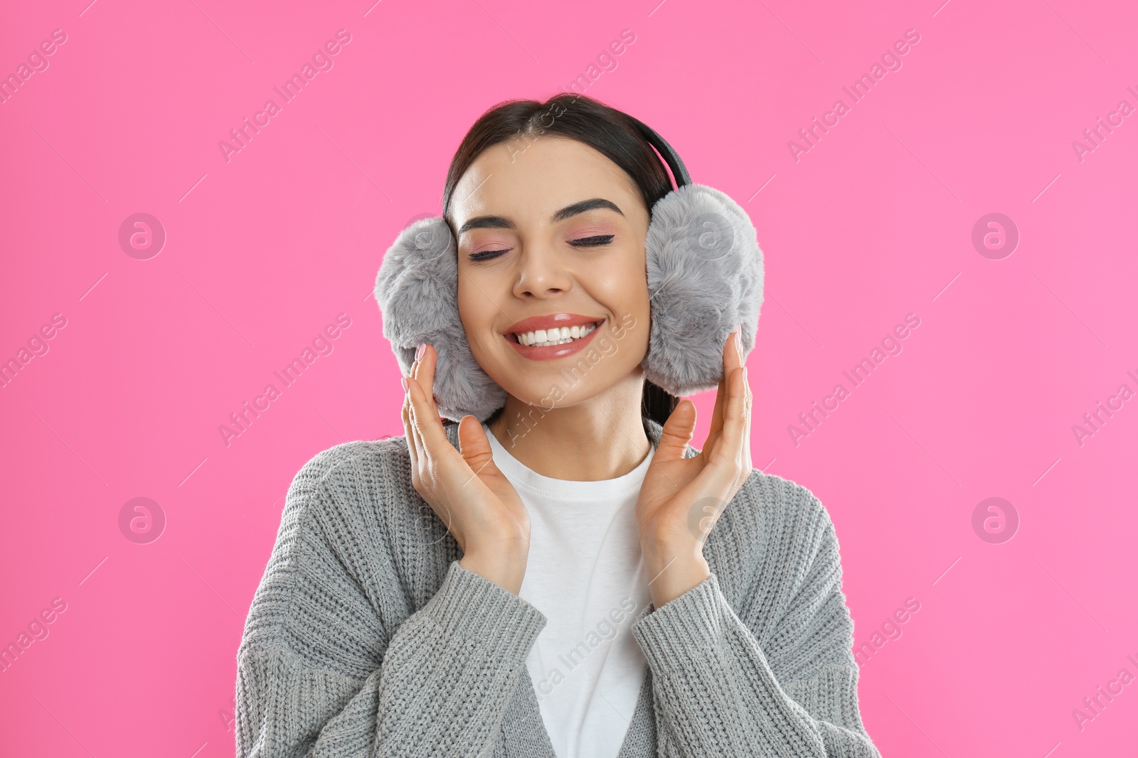 Photo of Beautiful young woman wearing earmuffs on pink background