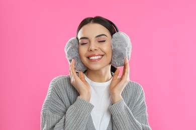 Beautiful young woman wearing earmuffs on pink background