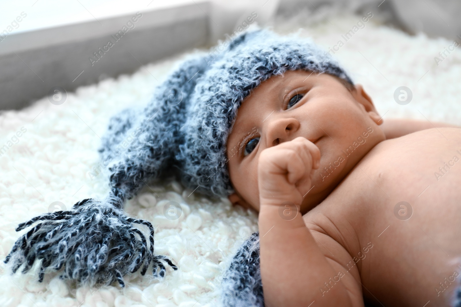 Photo of Cute little baby in grey hat lying on soft blanket