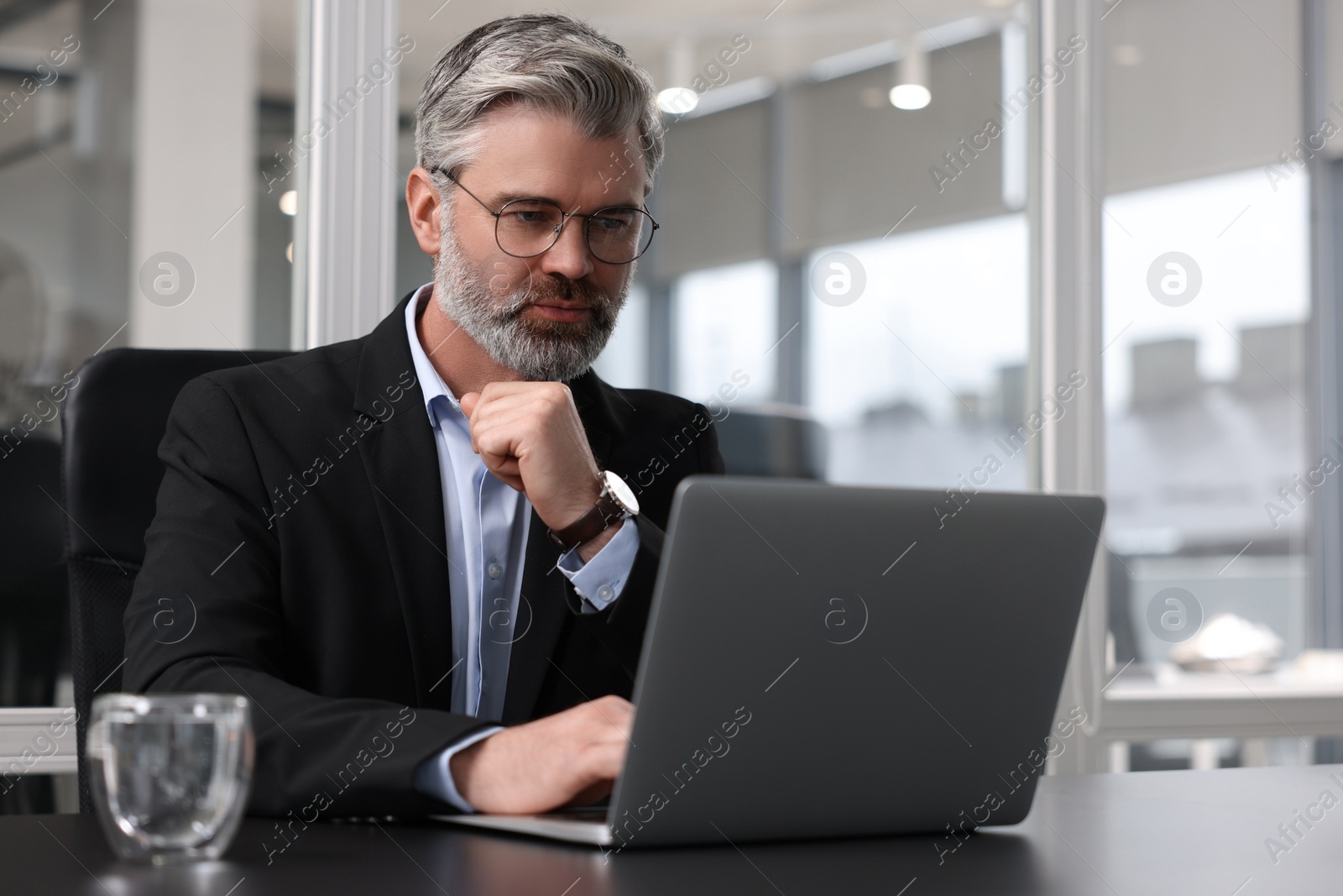Photo of Handsome man working with laptop at table in office. Lawyer, businessman, accountant or manager
