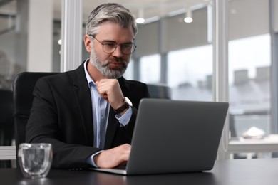 Handsome man working with laptop at table in office. Lawyer, businessman, accountant or manager