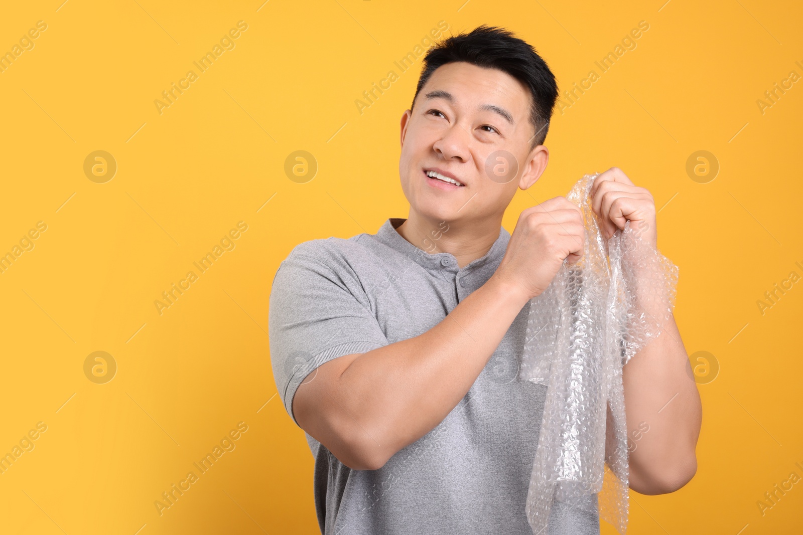 Photo of Asian man with bubble wrap on orange background. Space for text