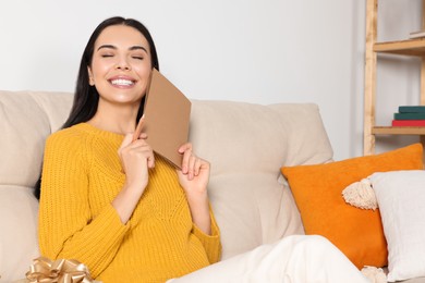 Happy woman holding greeting card on sofa in living room