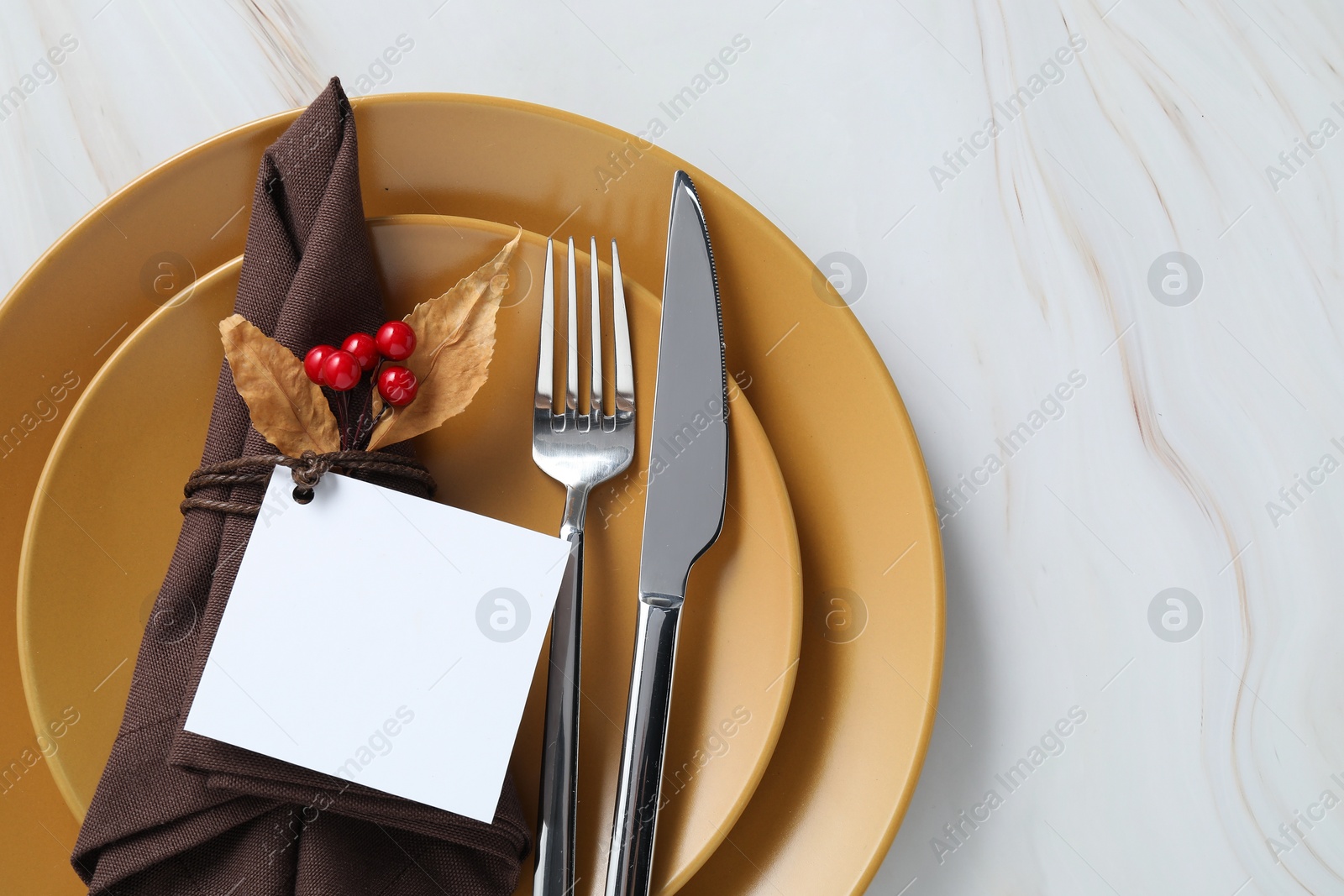 Photo of Thanksgiving table setting. Plates, cutlery, napkin, empty card and autumn decor on white marble background, top view, Space for text