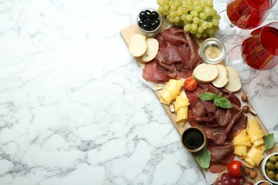Photo of Charcuterie board. Delicious bresaola, wine and other products on white marble table, flat lay. Space for text