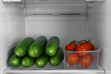 Photo of Cucumbers and tomatoes on shelf in refrigerator