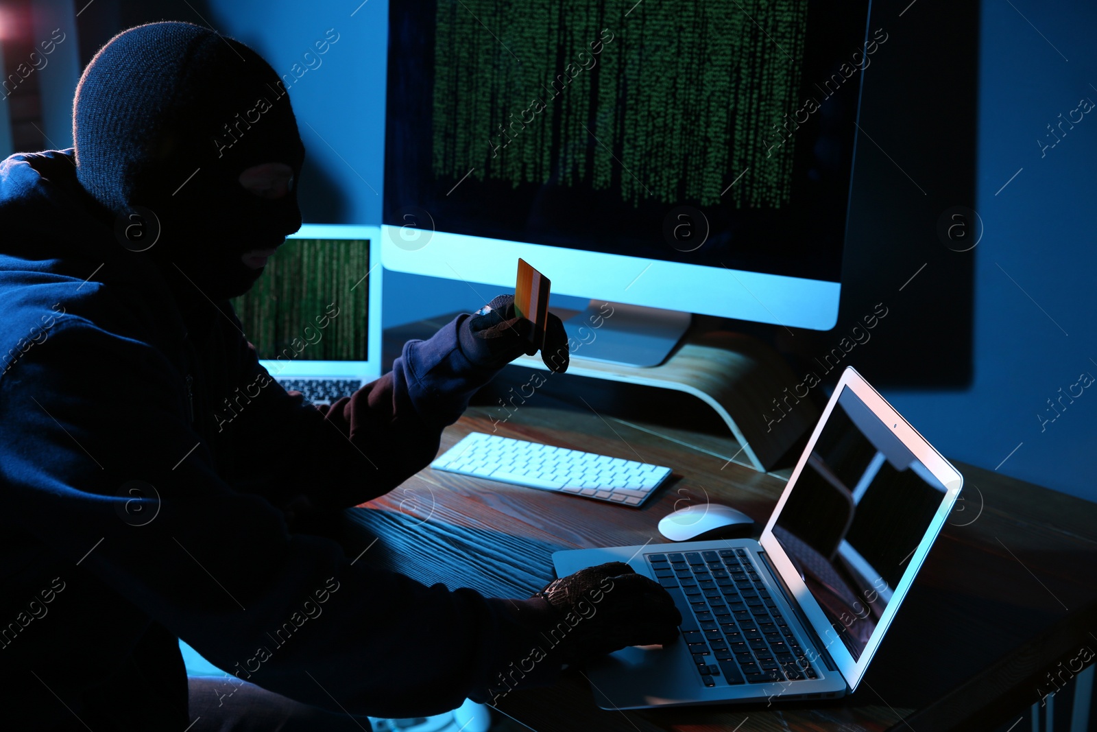 Photo of Hacker with credit card and laptop in dark room. Cyber crime