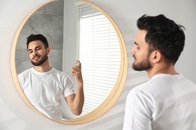 Man spraying luxury perfume near mirror indoors