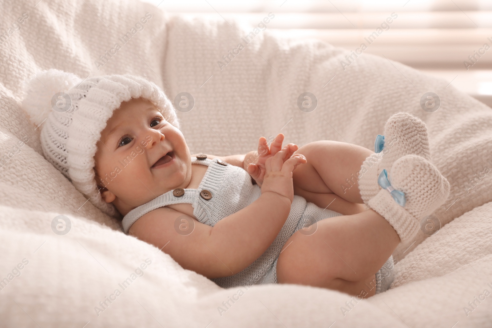 Photo of Cute little baby wearing white warm hat on knitted blanket