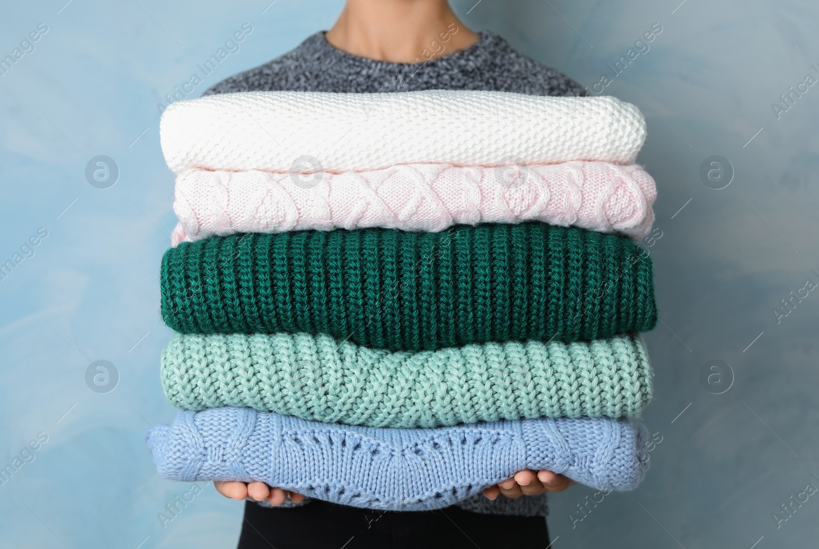 Photo of Woman holding stack of warm clothes on light blue background, closeup. Autumn season