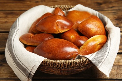 Photo of Delicious baked pirozhki in wicker basket on wooden table