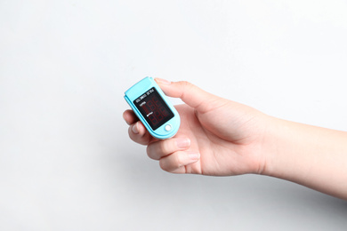 Woman holding fingertip pulse oximeter on white background, closeup