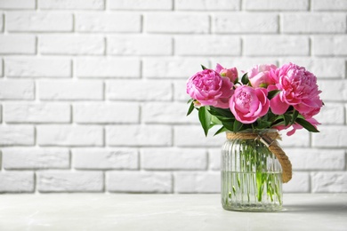 Vase with beautiful peony flowers on table against brick wall