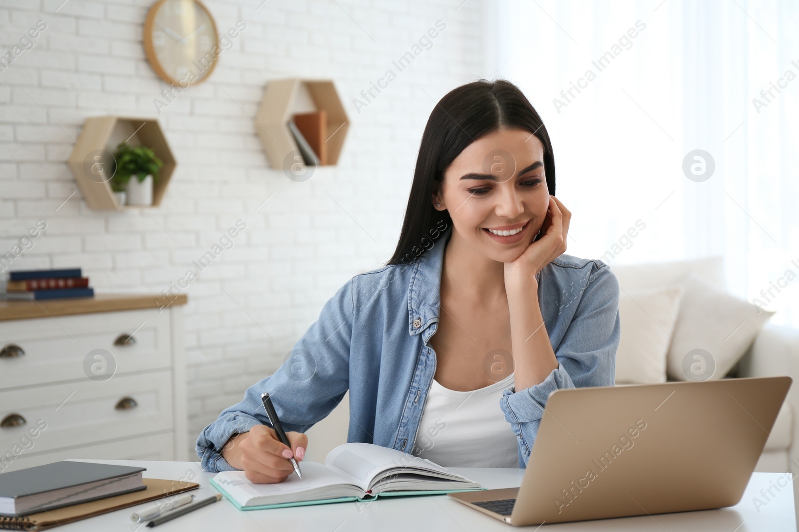 Photo of Young woman taking notes during online webinar at table indoors