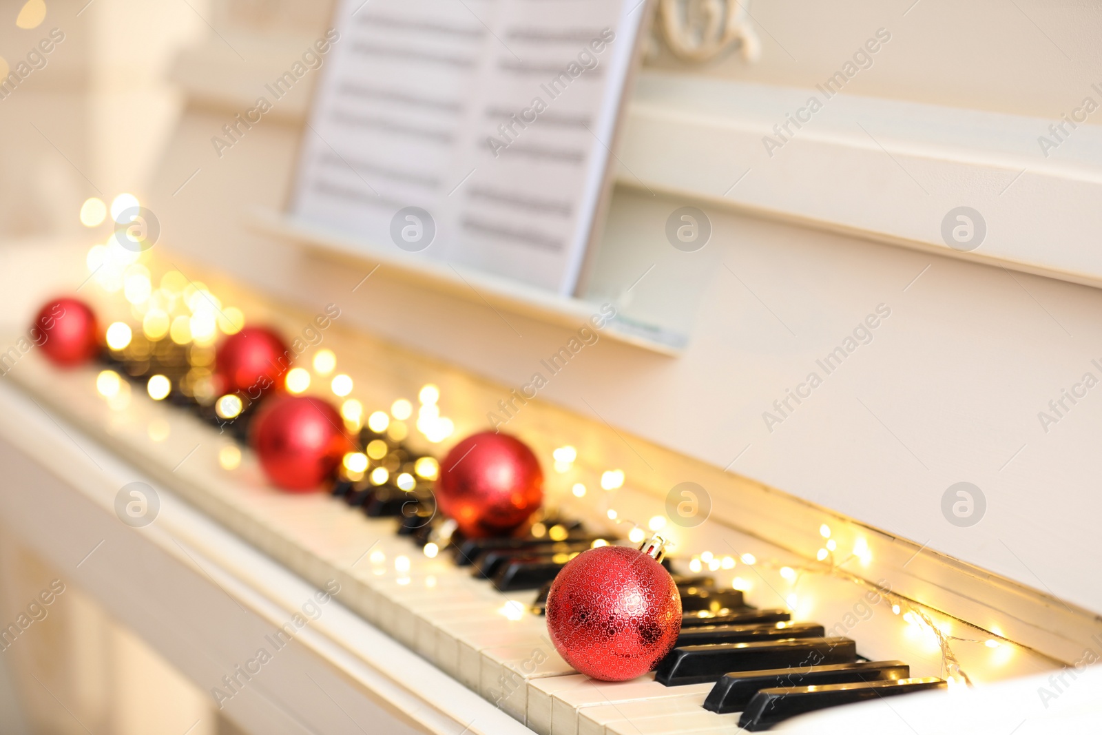 Photo of Red baubles and fairy lights on piano keys, closeup. Christmas music