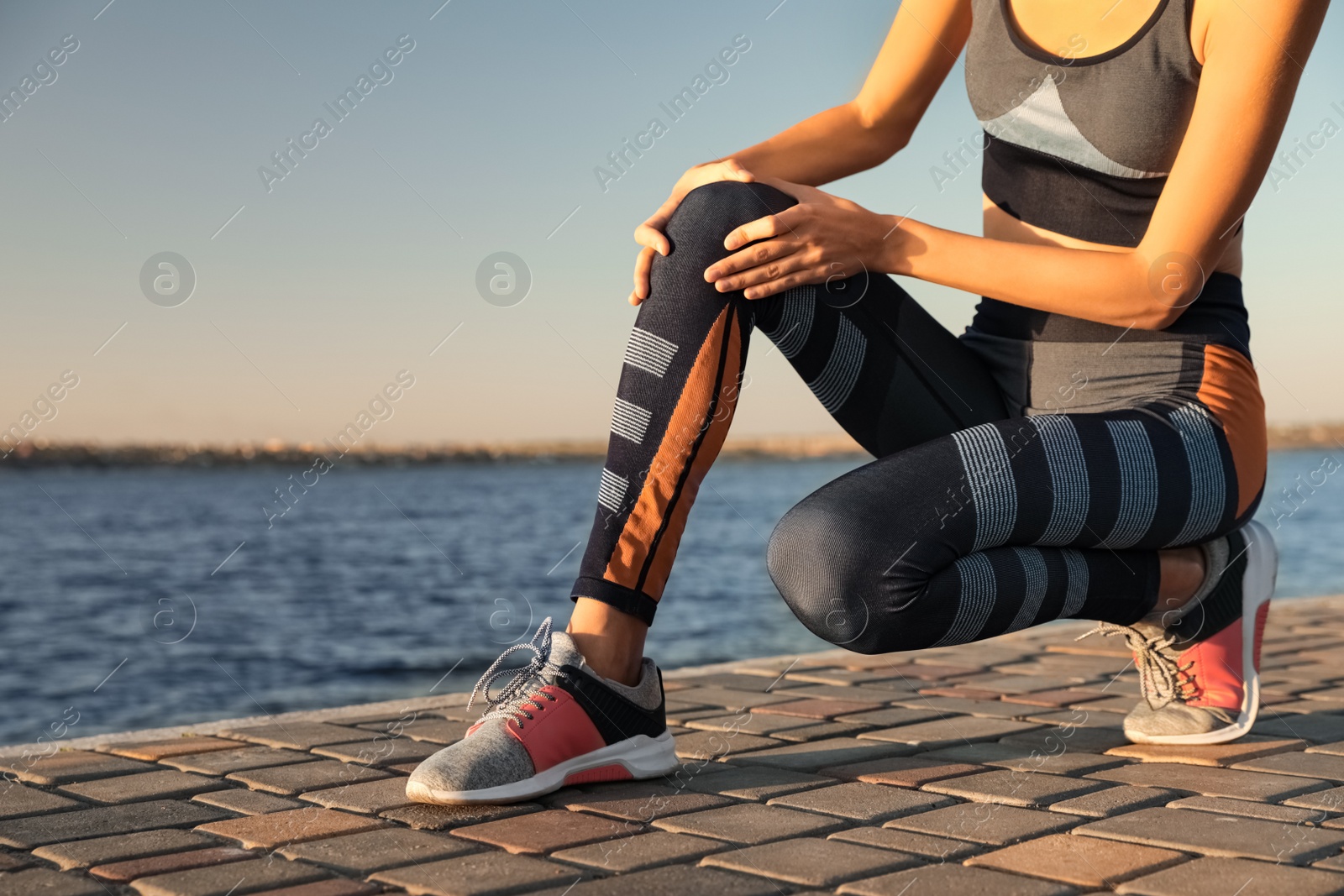 Photo of Young woman in sportswear having knee problems near river at sunset, closeup