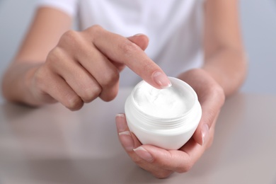 Photo of Young woman holding jar of cream at table, closeup