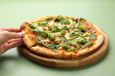 Photo of Woman taking piece of delicious vegetarian pizza at green table, closeup