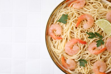 Photo of Tasty spaghetti with shrimps, lime and parsley in bowl on white tiled table, top view. Space for text